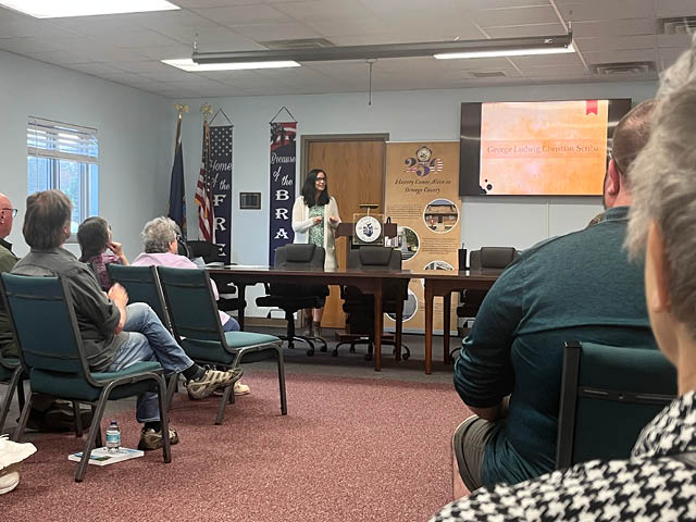 A photo of Christene Kieffer presenting to a crowded room at the Scriba Municipal Building