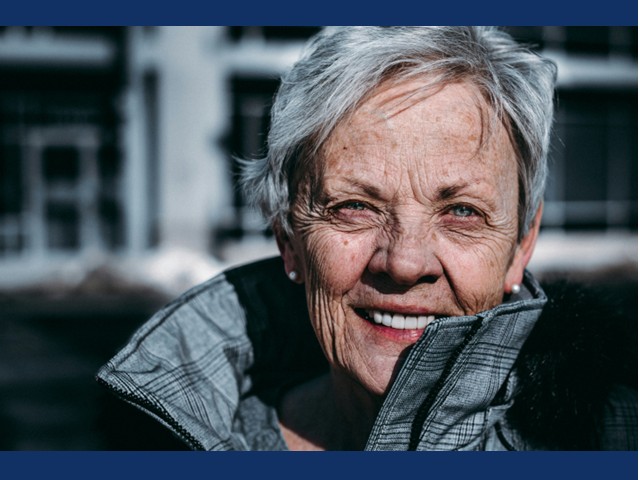 Older woman with short gray hair, collar on gray coat pointed up.