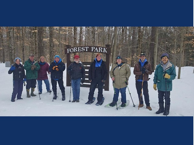 Nine hikers some with snow shoes in front of Forest Park sign.