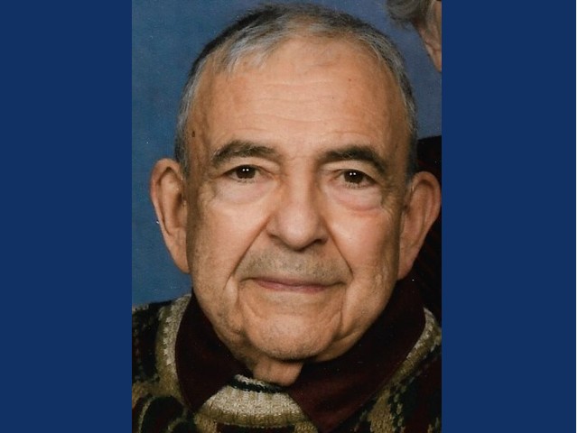 Older man with gray hair with slight grin wearing brown collared shirt.
