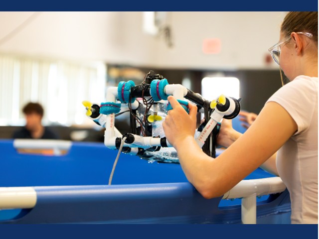 Young students holding an ROV on the side of a blue pool.