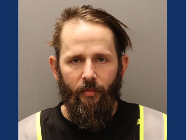 Man with short dark hair parted on side with beard and mustache