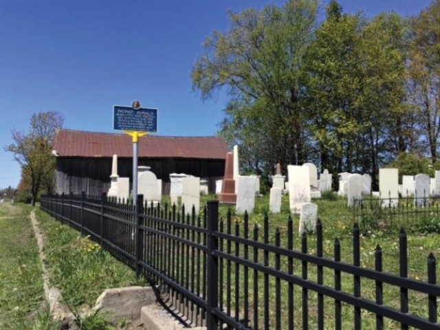 Photo: A cemetery in the summer with a patriotic burial marker visible but unreadable in the distance