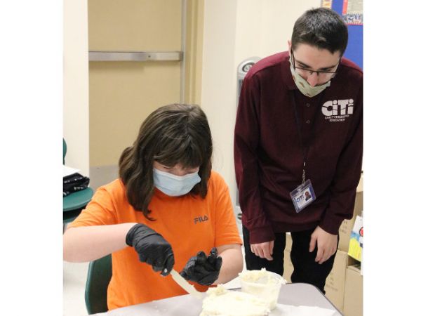 Cian O’Neil (Mexico Academy &amp; Central School District), an Early Childhood Education student at the Center for Instruction, Technology &amp; Innovation, awaits to provide CiTi student Jade Duffield additional helpful ways to decorate a holiday cake, provided by CiTi’s Culinary Arts students.